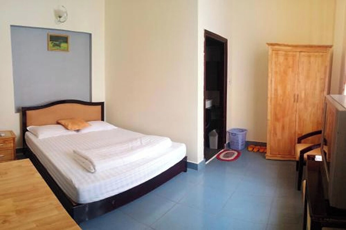 A bedroom with a bed, a wooden wardrobe, a desk, and a chair.