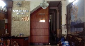 El interior del hotel Khach San, con un mostrador de recepción, una pared de madera con un letrero y un cuadro de un paisaje montañoso.