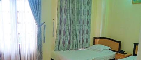 A room with two beds, a window with sheer curtains, an air conditioning unit, and a bedside table with a lamp.