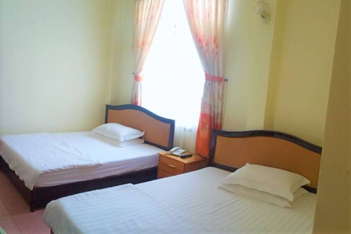 Une chambre d’hôtel avec deux lits simples, une table de chevet avec un téléphone et une fenêtre avec des rideaux.