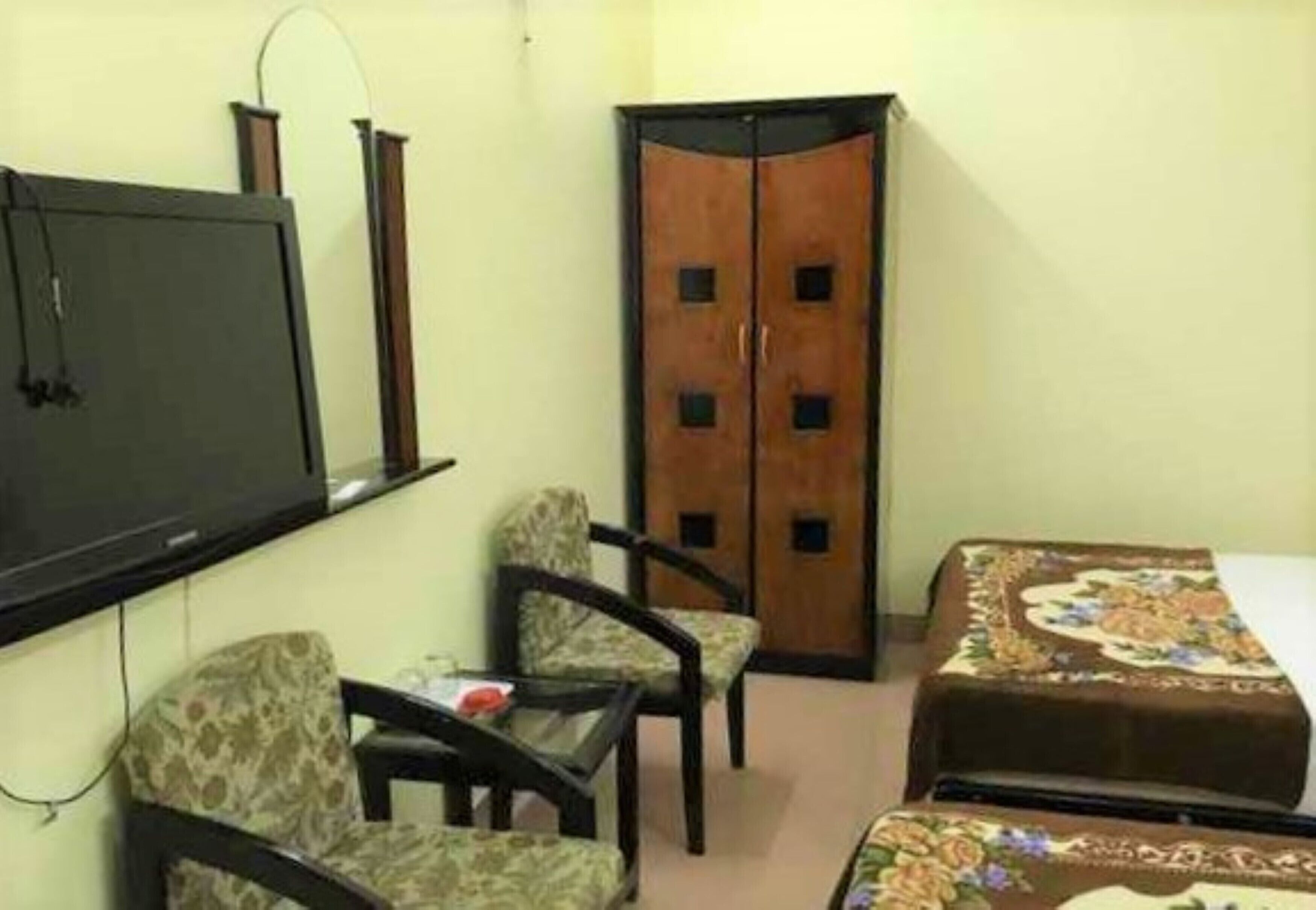 A small room with a bed, a TV, a wardrobe, and two chairs.