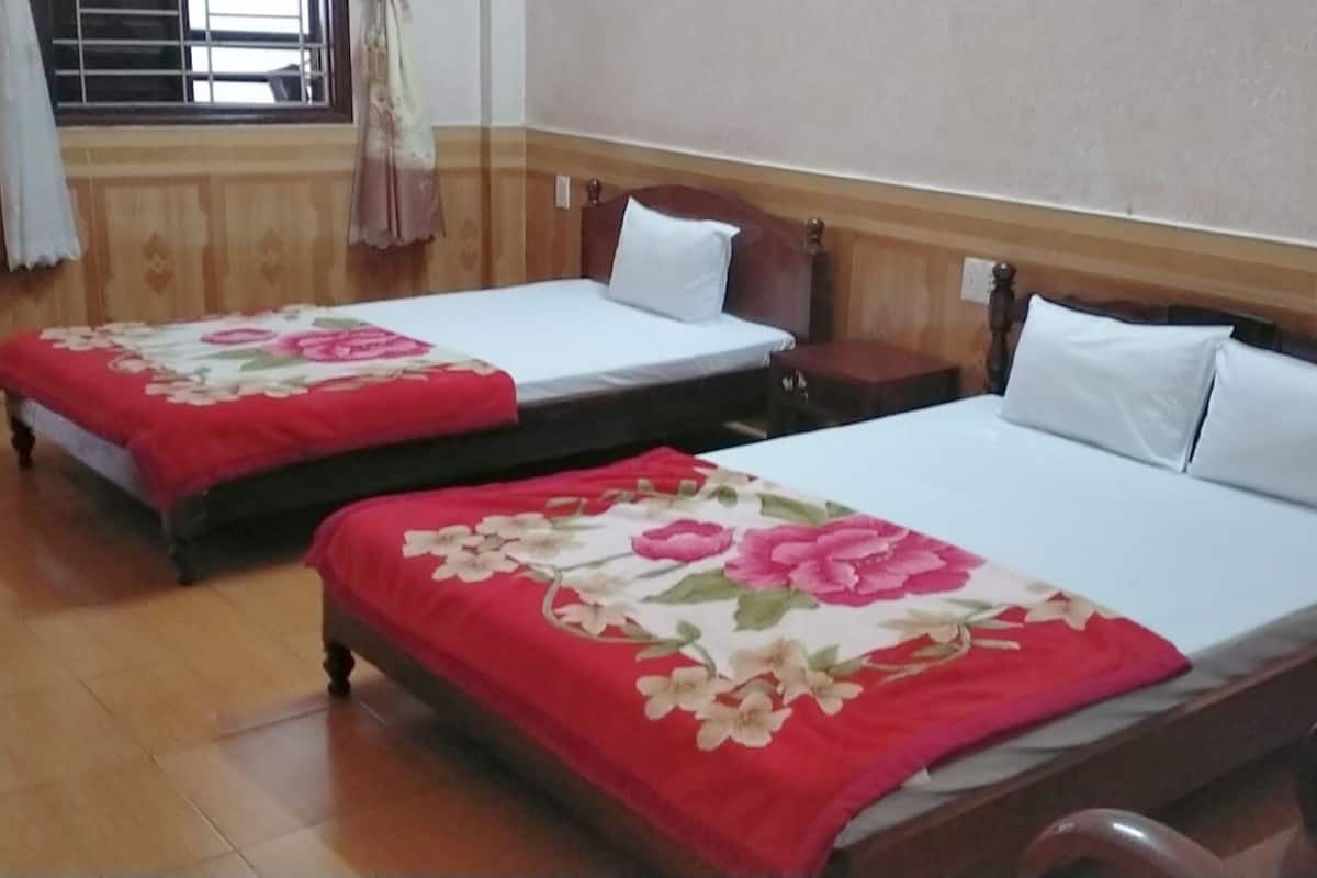 Deux lits simples avec des couvre-lits à motifs floraux, des têtes de lit en bois et des oreillers blancs, dans une pièce dotée d’un plancher en bois et d’une fenêtre avec des rideaux.