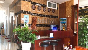 Een hotel receptie met een marmeren muur, klokken die verschillende steden weergeven, een receptiebalie en een bar met krukjes.