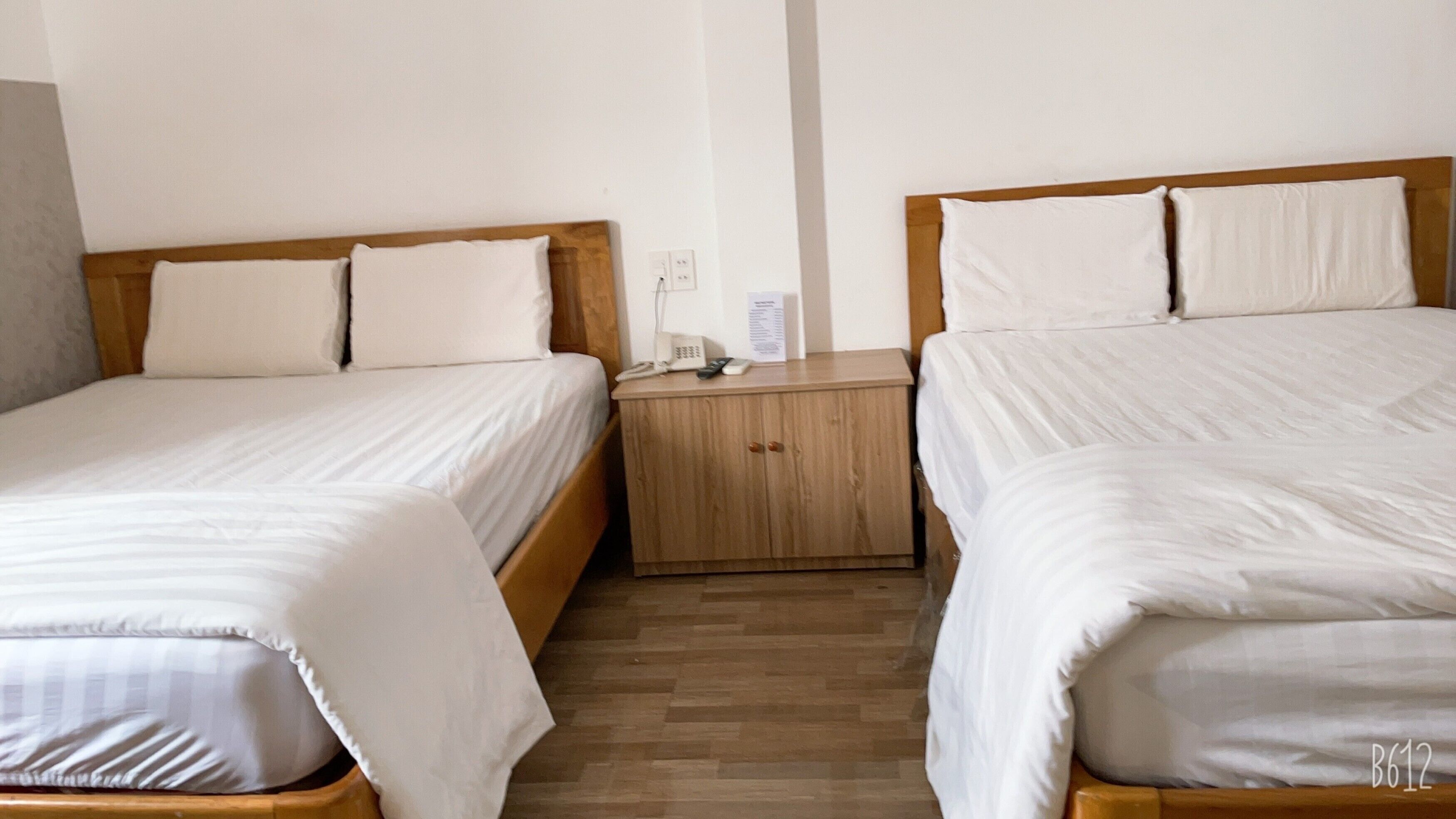 Una habitación de hotel con dos camas individuales, una mesita de noche de madera con un teléfono y un control remoto, y suelo de madera.
