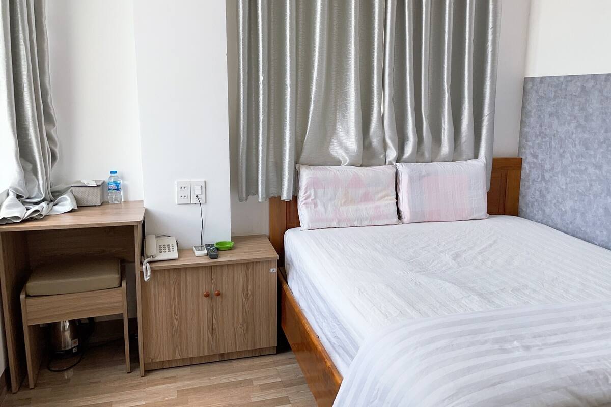 A hotel room with a wooden desk, a telephone, a green bowl, and a bed with a grey headboard.