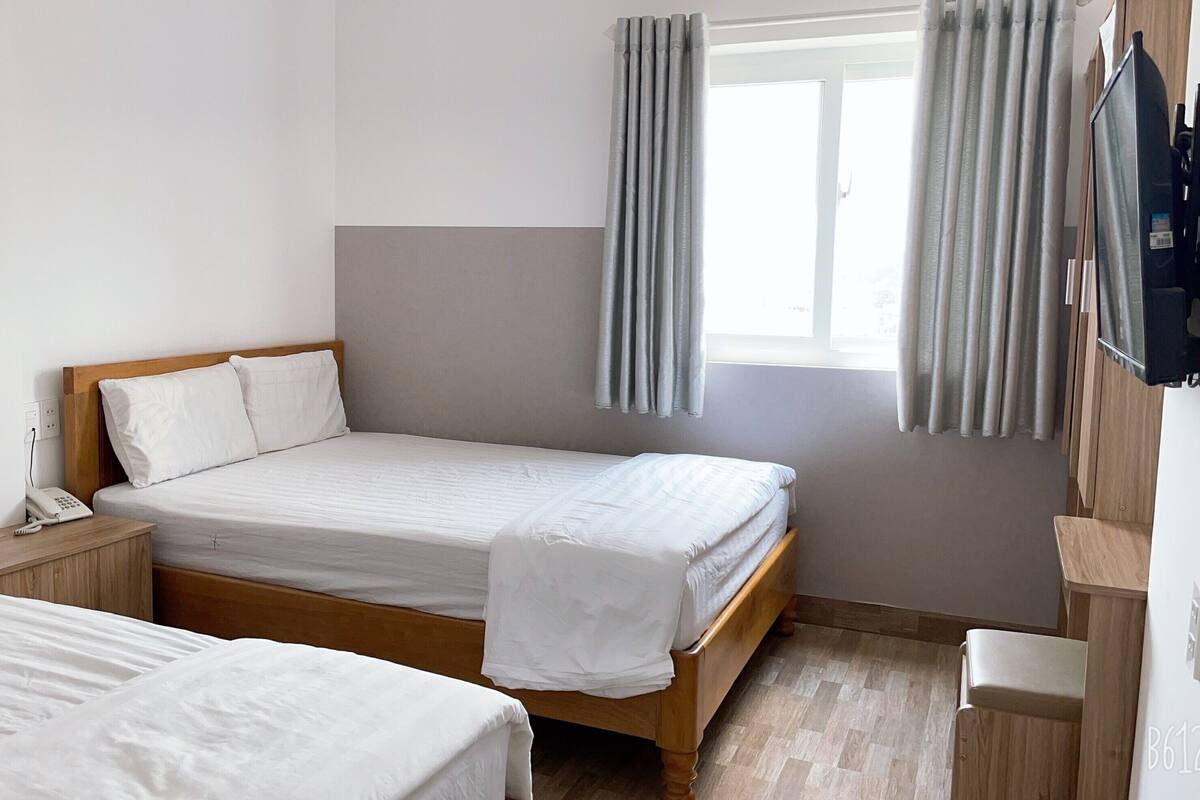 A hotel room with a single bed, a bedside table with a phone and a water bottle, and a window with curtains.