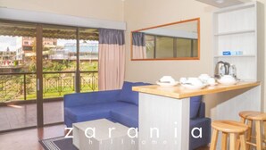 A modern living room with a blue sofa, a wooden coffee table, and a kitchen area with a counter and stools. - Zarania Hillhomes Cameron Highlands (Brinchang)