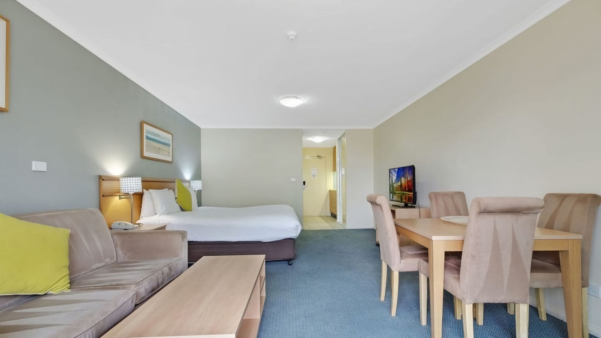 Una habitación de hotel con una cama, un sofá, una mesa de comedor con sillas, un televisor y un cuadro en la pared.