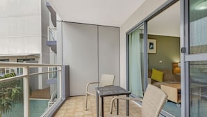 Ein Balkon mit Glastür, zwei Korbstühle, ein kleiner Tisch und Blick auf ein Schlafzimmer mit Bett und Lampe.