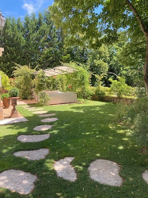 Un jardín con césped, piedras para caminar y un pérgola.