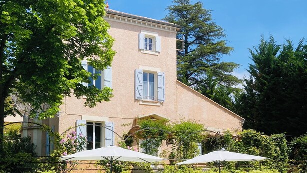 A swimming pool with lounge chairs and umbrellas, surrounded by greenery and a building with shutters. - The Bastide of Villecroze  (Villecroze)