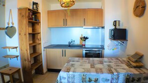A compact kitchen with wooden cabinets, a microwave, and a table with a quilted tablecloth. - 6 pers- plagne center, Montblanc view, telebus base. (LA PLAGNE)