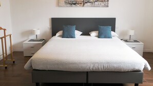 Een keurig opgemaakte hotelkamer met een groot bed, twee nachtkastjes, een houten stoel en een stadsgezichtschilderij aan de muur.