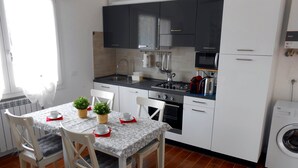Een compacte keuken met witte kasten, een eettafel met stoelen, een koffiezetapparaat en een wasmachine.