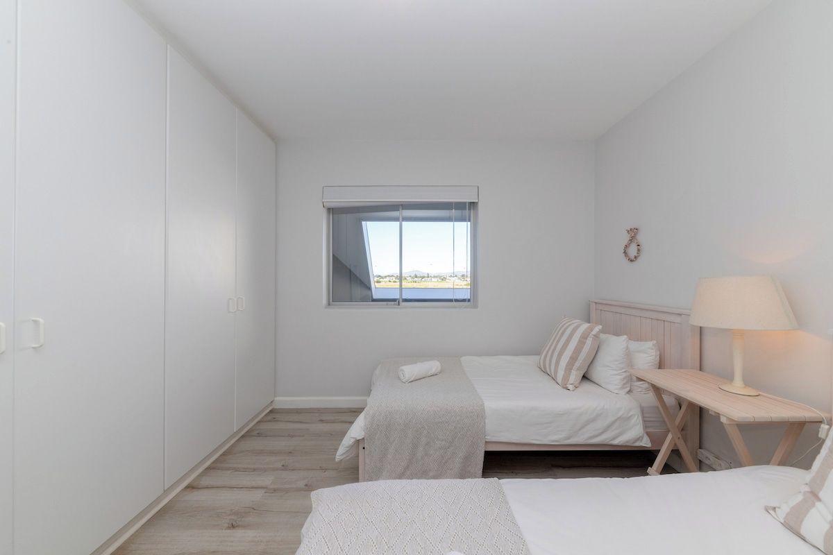 Ein Schlafzimmer mit zwei Betten, einem Fenster, einem Nachttisch mit Lampe und Blick ins Freie.