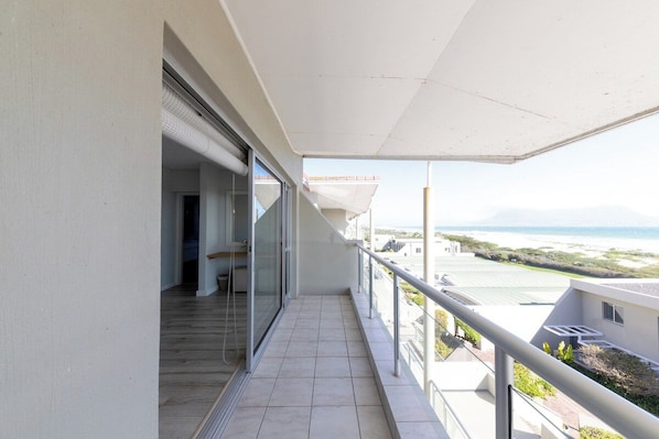 A balcony with a view of the sea, a glass door leading to an interior space, and a tiled floor.