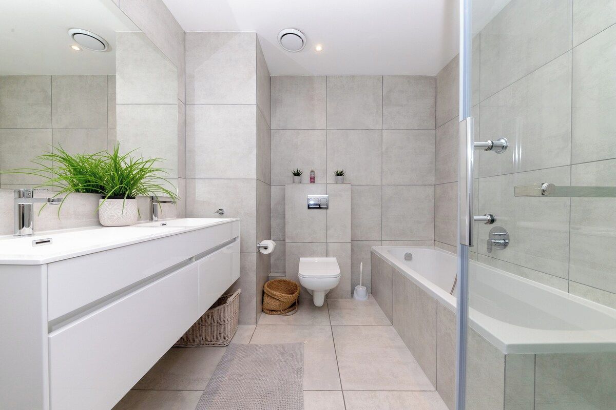 A modern bathroom with a large mirror, white vanity, a toilet, and a bathtub.