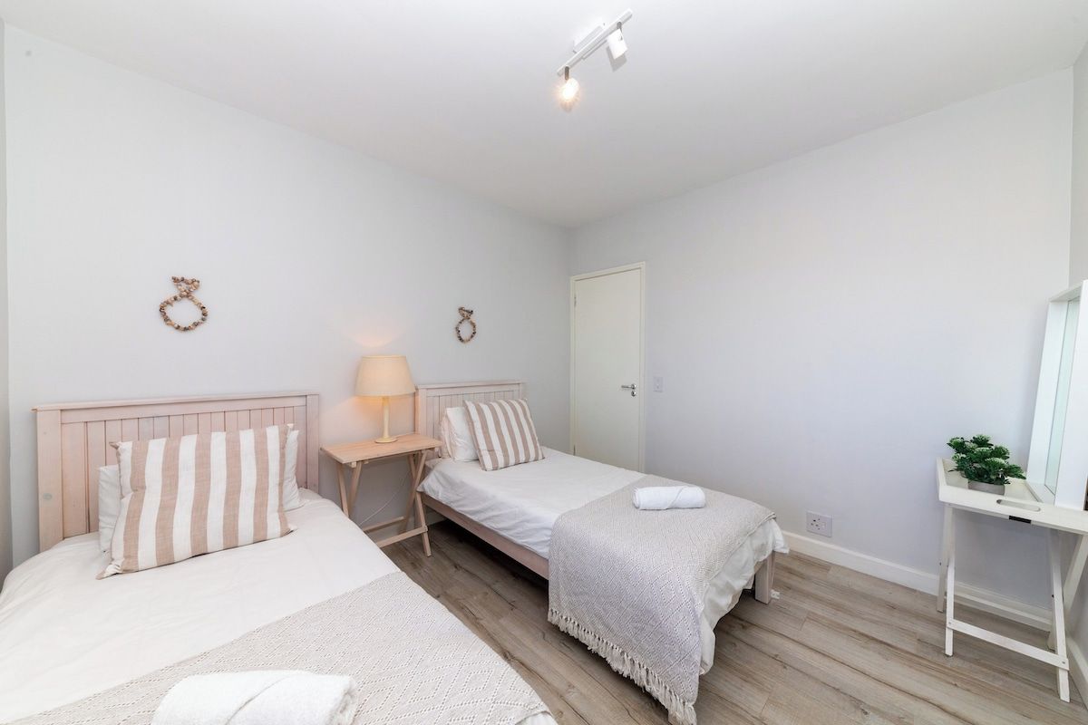 Un dormitorio con dos camas, una mesita de noche con lámpara, un armario y un espejo sobre un pedestal.