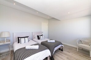 A bedroom with two beds, a bedside table with a lamp, a wicker chair, and a door.