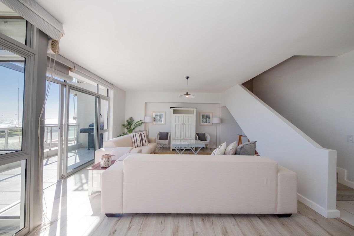 A spacious living area with a large sofa, a dining table, and a staircase.