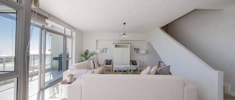 A spacious living area with a large sofa, a dining table, and a staircase.