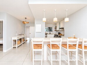 A modern kitchen with white cabinetry, a dining area with white tables and chairs, and pendant lighting.