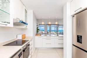 A modern kitchen with white cabinetry, a built-in oven, and a view to the outside. - Dolphin Beach C110 Beachfront Beauty by hmh (Cape Town)