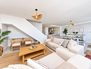 A modern living room with a sofa, chairs, a wooden coffee table, and a staircase.