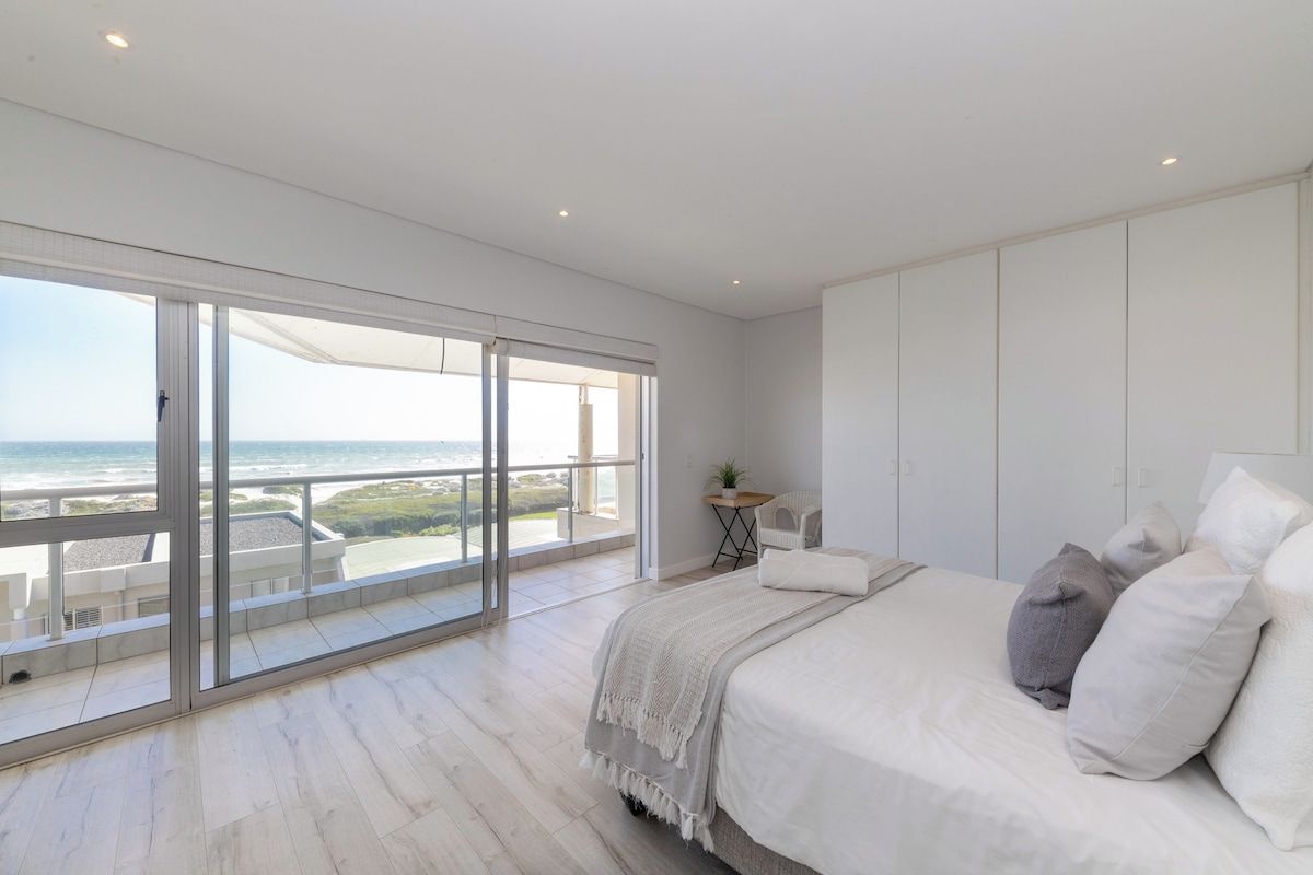 Un dormitorio con un amplio ventanal corredera que da a un balcón con vistas al mar.