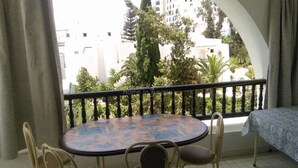 Een balkon met een ronde tafel en stoelen, uitzicht op een stadsgezicht, en een overdekt gedeelte met een tafelkleed met patroon.