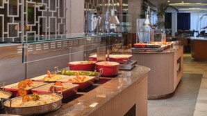 A buffet area with various food stations, a modern interior design, and a seating area in the background. - Atlantica Oasis (Limassol)