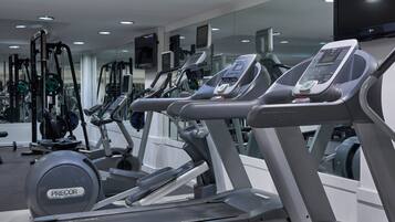 Uma academia com várias esteiras, aparelhos de musculação e um espelho grande.