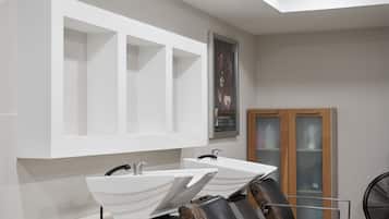 Ein moderner Friseursalon mit zwei Waschbecken, einer Holztruhe und einem schwarzen Ventilator.