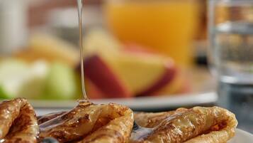 A plate of pancakes with syrup being poured over them, accompanied by blueberries and a glass of orange juice.