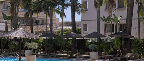 A poolside area with palm trees, lounge chairs, and umbrellas.