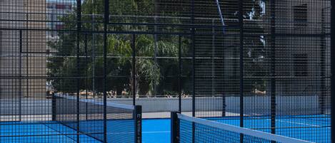 A tennis court with a net, surrounded by a metal fence.
