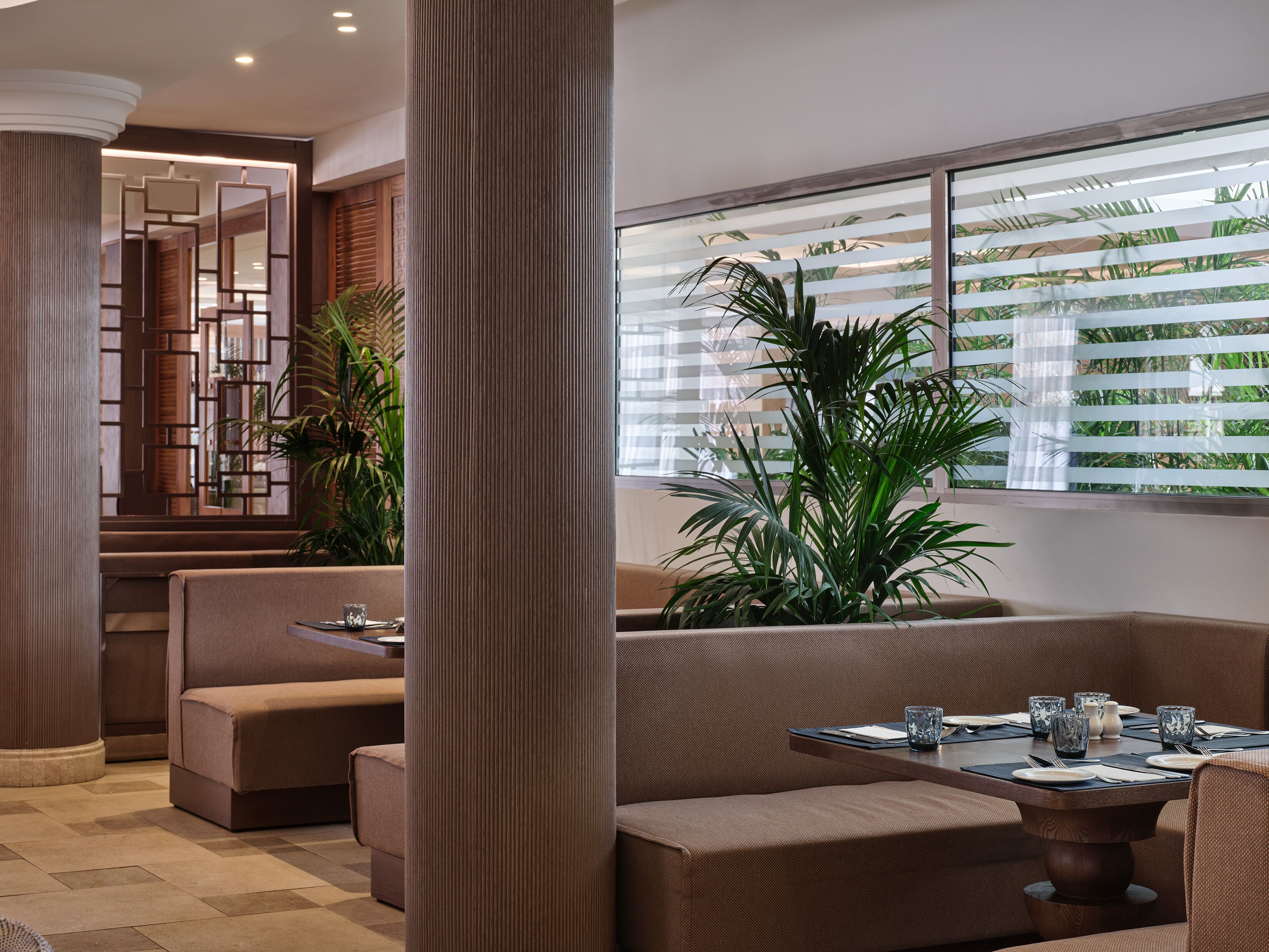 A modern interior with a seating area, a dining table, and large windows with blinds.