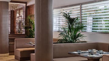 Un interior moderno con una zona de estar, una mesa de comedor y ventanas grandes con persianas.
