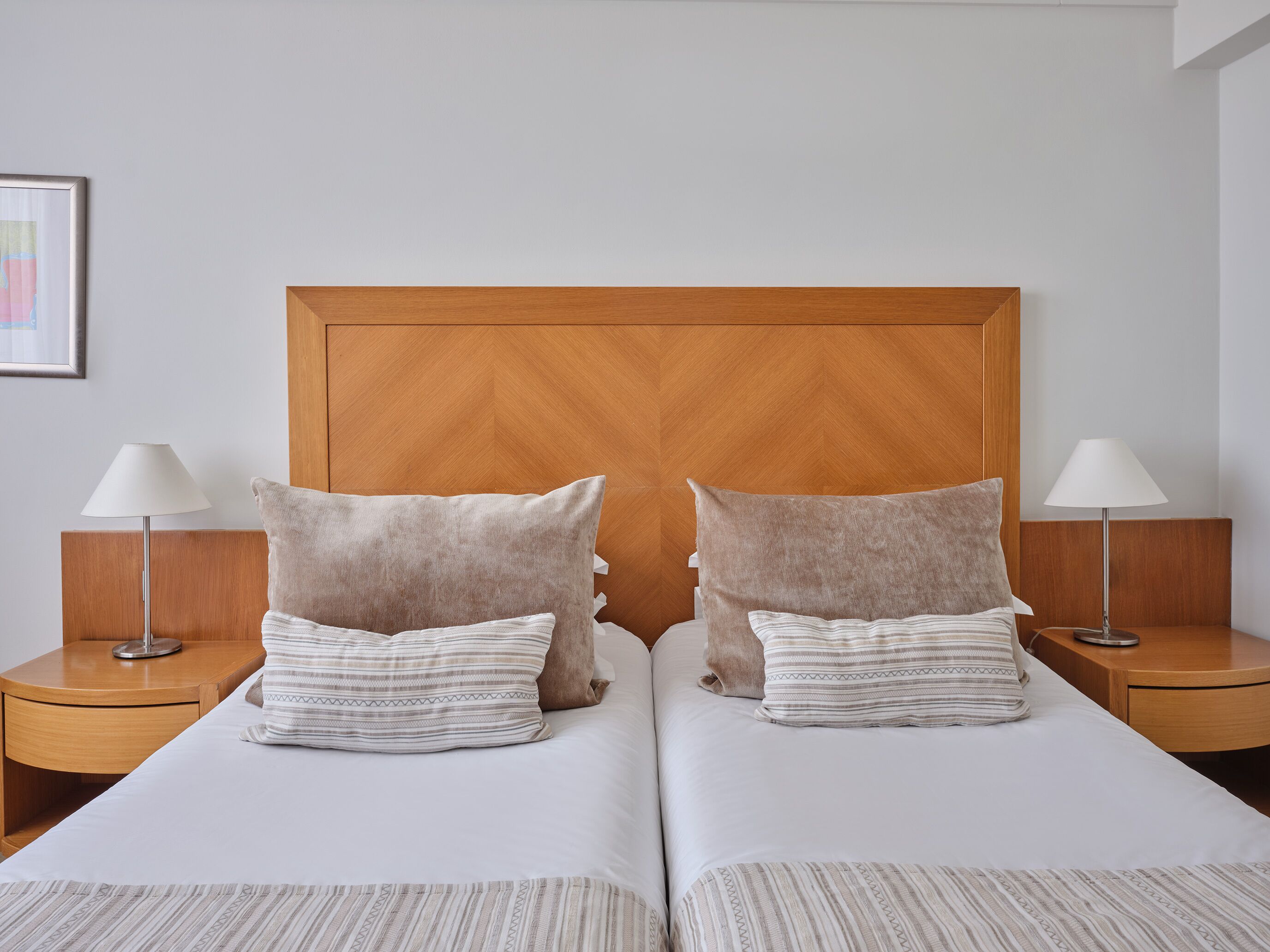 A hotel room with two beds, wooden headboard, bedside lamps, and a framed picture on the wall.