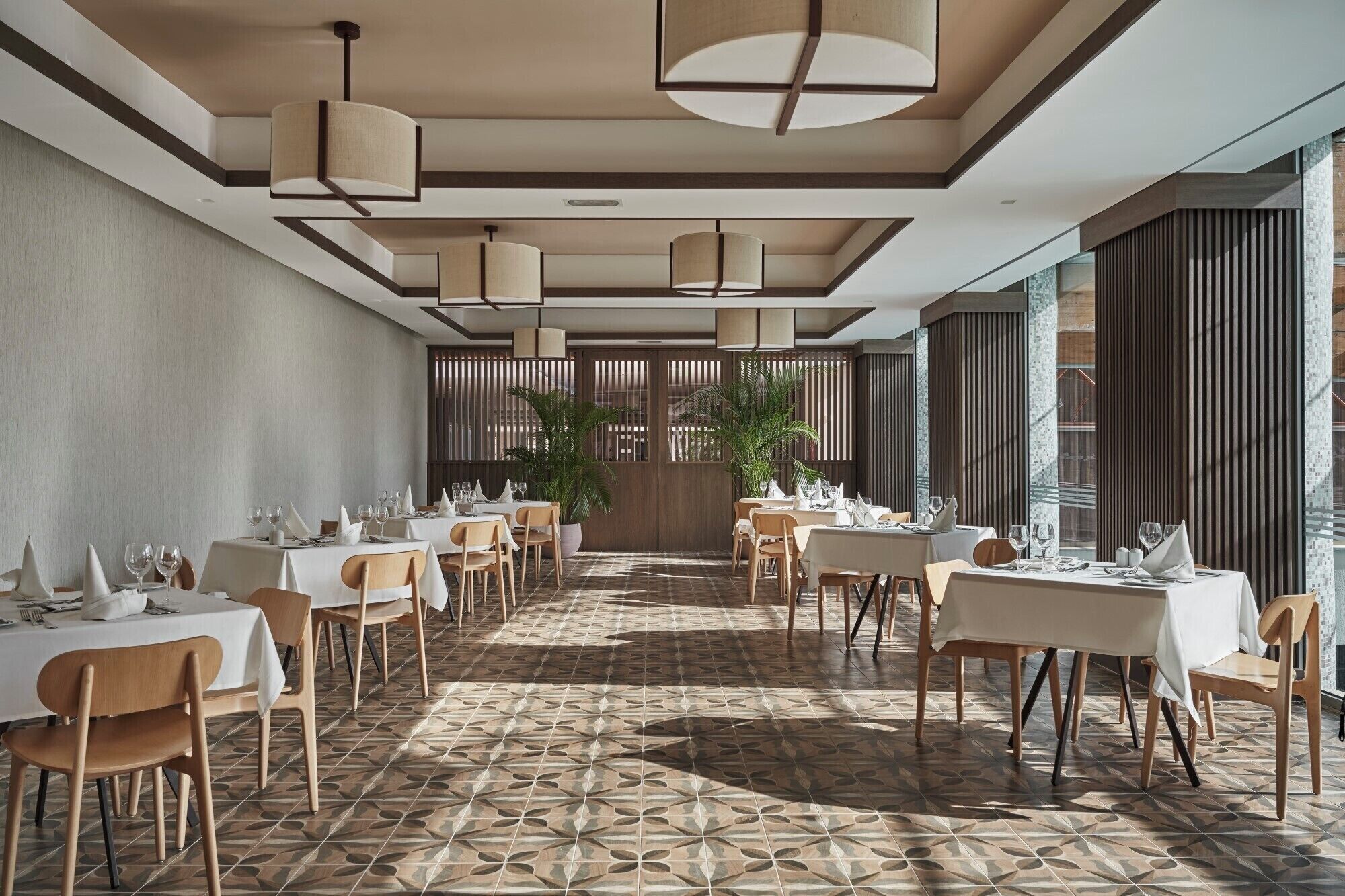 A spacious dining area with multiple tables and chairs, a patterned floor, and large windows.