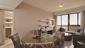 A modern living room with a glass-top dining table, patterned sofas, and a view of the sea through large windows.