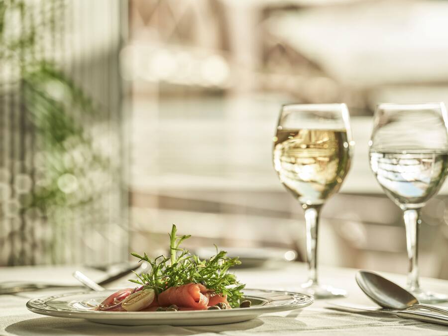 A dining table with two glasses of white wine, a plate with a food item, and a spoon.