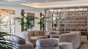 A modern lobby with a seating area featuring grey upholstered sofas and a decorative partition with geometric patterns. - Atlantica Oasis (Limassol)