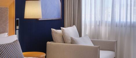 A hotel room with a bed, a sofa, a lamp, a painting, and a window with curtains.
