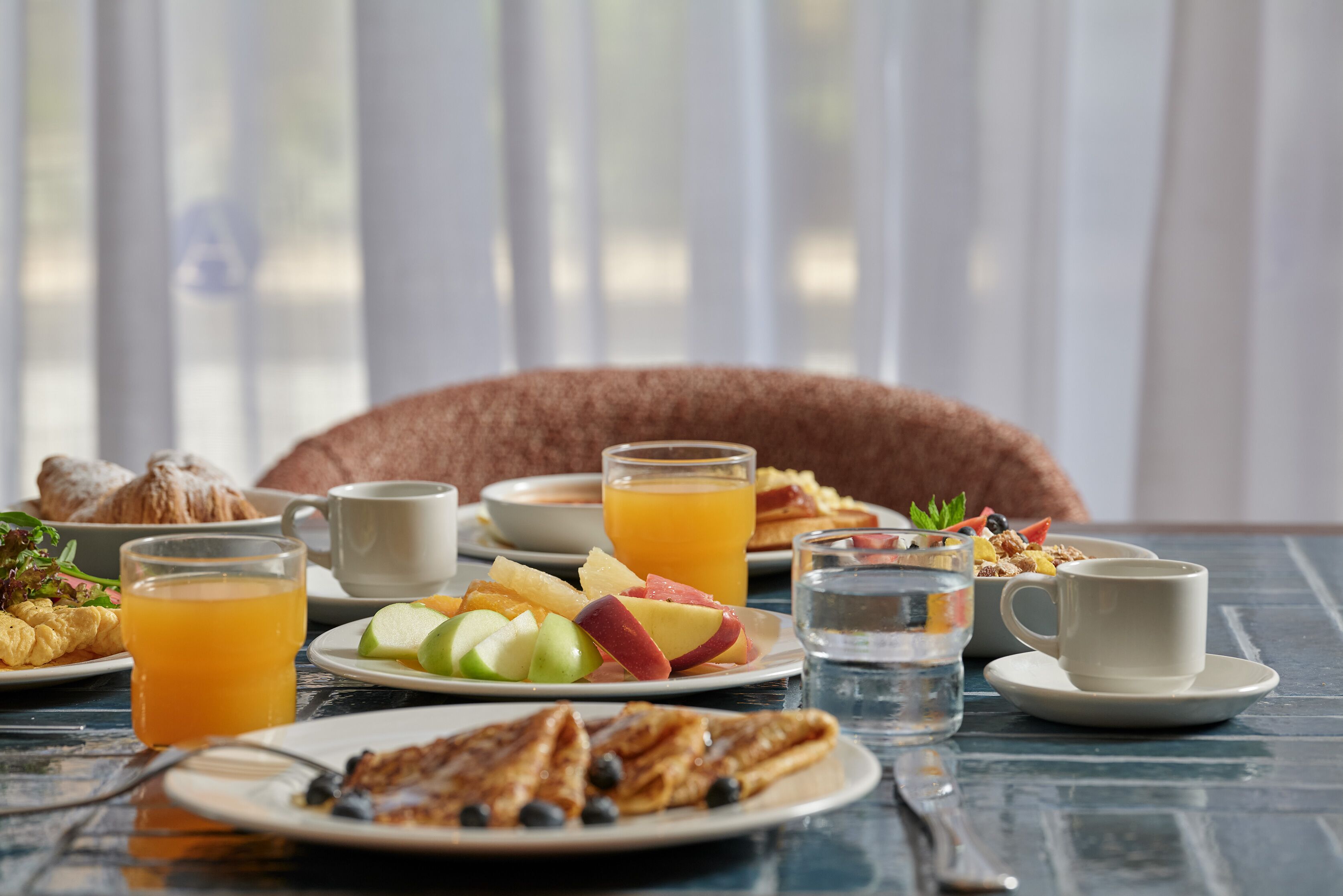 A breakfast table with plates of food, glasses of orange juice, and a cup of coffee.