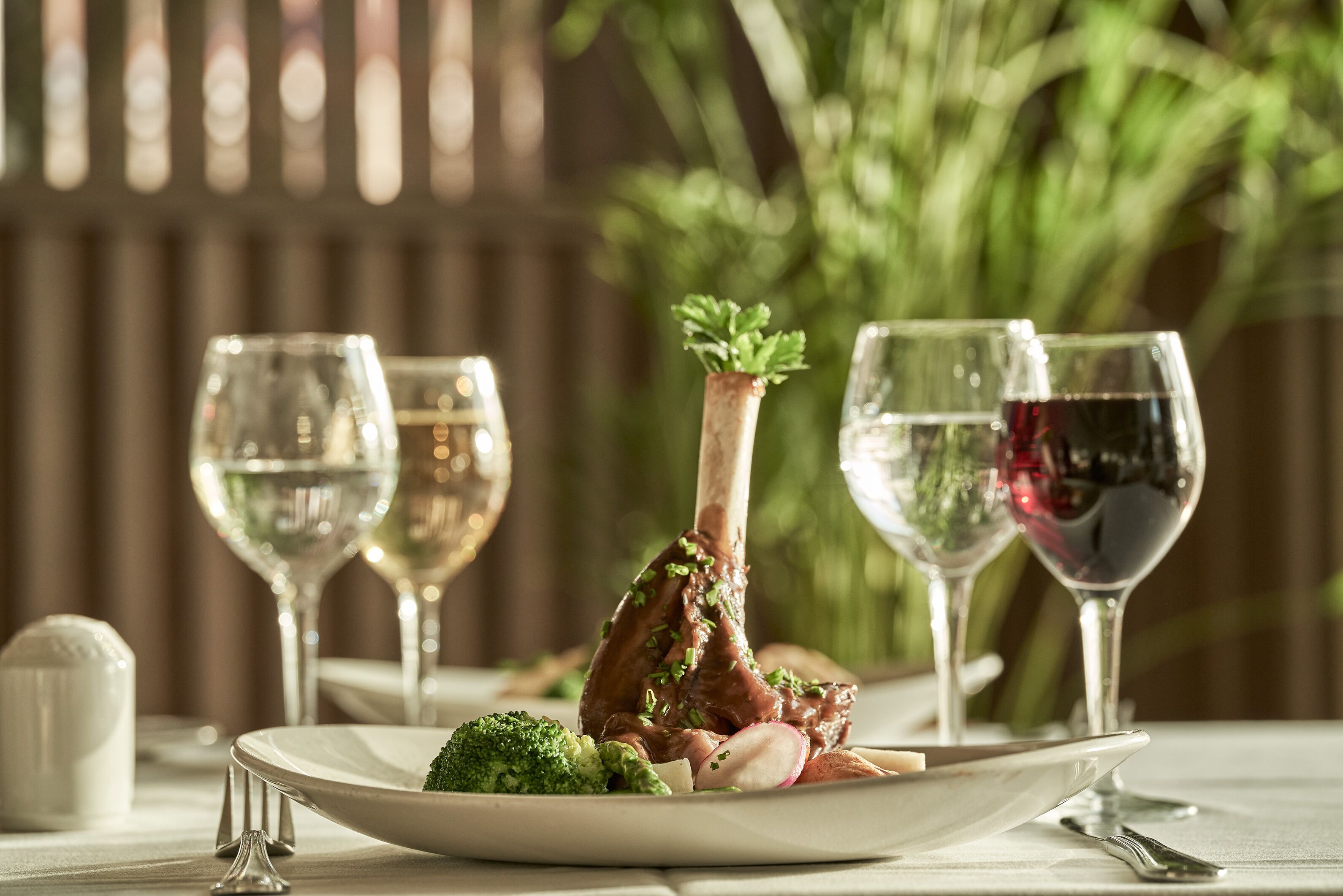 A dining table with a plate of food, two wine glasses, and a decorative plant.