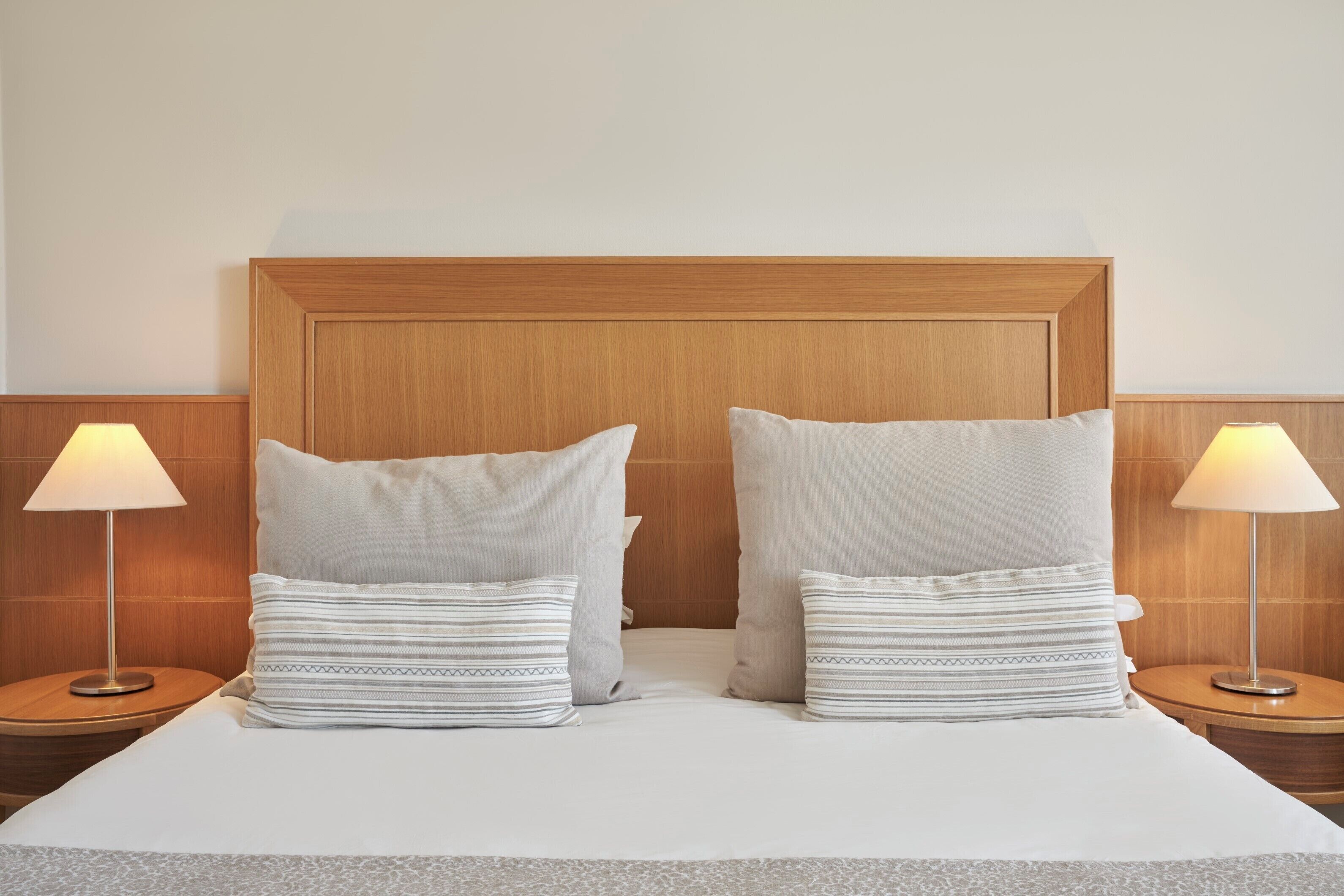 A neatly made bed with two pillows and two bedside lamps.