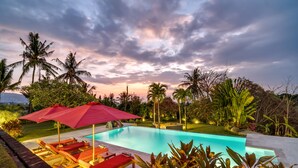 A swimming pool with lounge chairs and umbrellas, surrounded by tropical vegetation. - Villa Bloom by Villa Finder (Sukasada)
