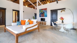A spacious bedroom with a wooden bed, a TV, and a dining area with a round table and chairs. - Villa Bloom by Villa Finder (Sukasada)