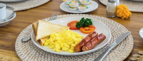 A breakfast plate with toast, scrambled eggs, sausages, and tomatoes on a woven placemat.